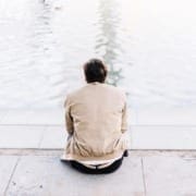 man sitting by water with back facing camera